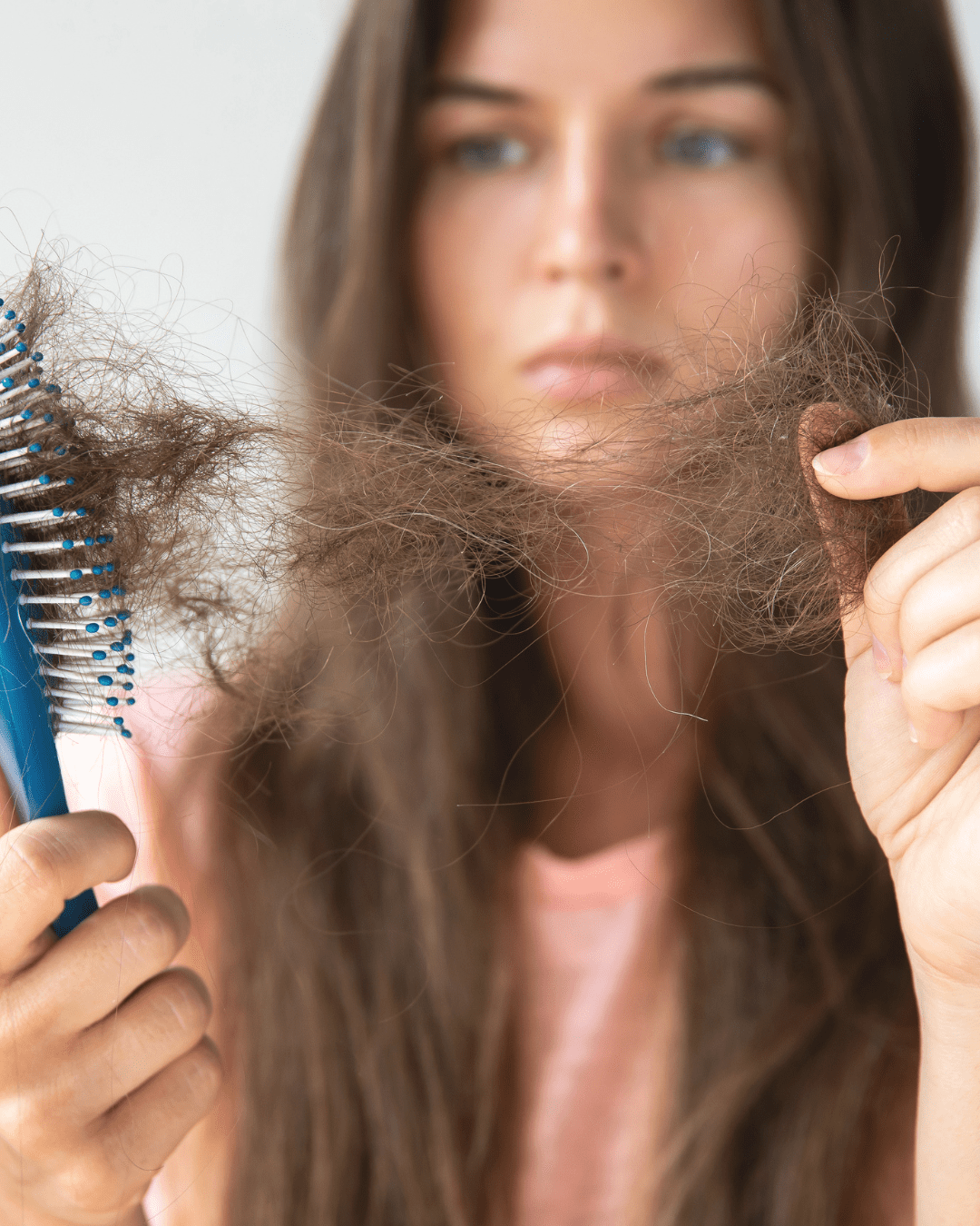 Mãe segurando mechas de cabelo caídas após o parto, olhando preocupada para os fios.
